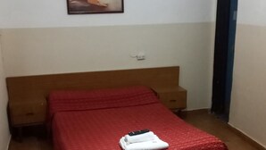 A bedroom with a single bed, a nightstand, a wall-mounted power outlet, and a door. - Hotel Florentino (Buenos Aires)