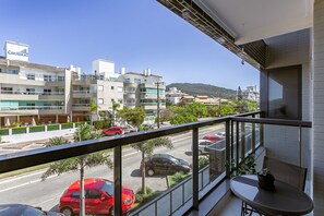 Un balcon donnant sur une rue, des immeubles et une colline au loin.