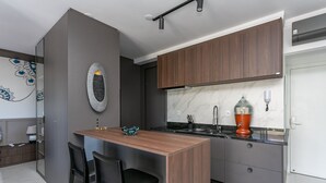 A modern kitchen with dark wood cabinets, a marble countertop, and a built-in island with two black chairs. - Luxurious Studio Right on the Sand in Irb203 (Florianópolis)