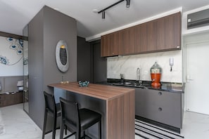 Une cuisine moderne avec des meubles en bois foncé, un plan de travail en marbre et un îlot central intégré, agrémenté de deux chaises noires.