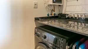 A compact laundry area with a front-loading washing machine, a dryer, and a drying rack. - Luxurious Studio Right on the Sand in Irb203 (Florianópolis)