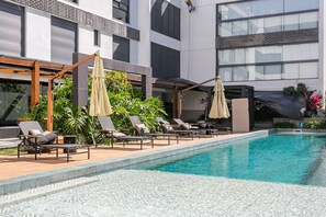 A modern pool area with lounge chairs and umbrellas, surrounded by a building with large windows and a brick facade. - Luxurious Studio Right on the Sand in Irb203 (Florianópolis)