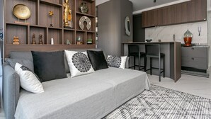 A modern living room with a grey sofa, patterned cushions, and a decorative shelf with various items. - Luxurious Studio Right on the Sand in Irb203 (Florianópolis)