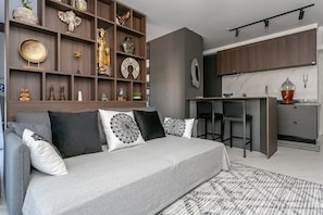 Een moderne woonkamer met een grijze bank, decoratieve kussens en een bijzettafeltje met diverse spullen.