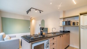 Une cuisine compacte équipée d’une cuisinière à gaz, d’un four à micro-ondes et d’un évier. Un petit coin salon avec un canapé et un fauteuil est également disponible.