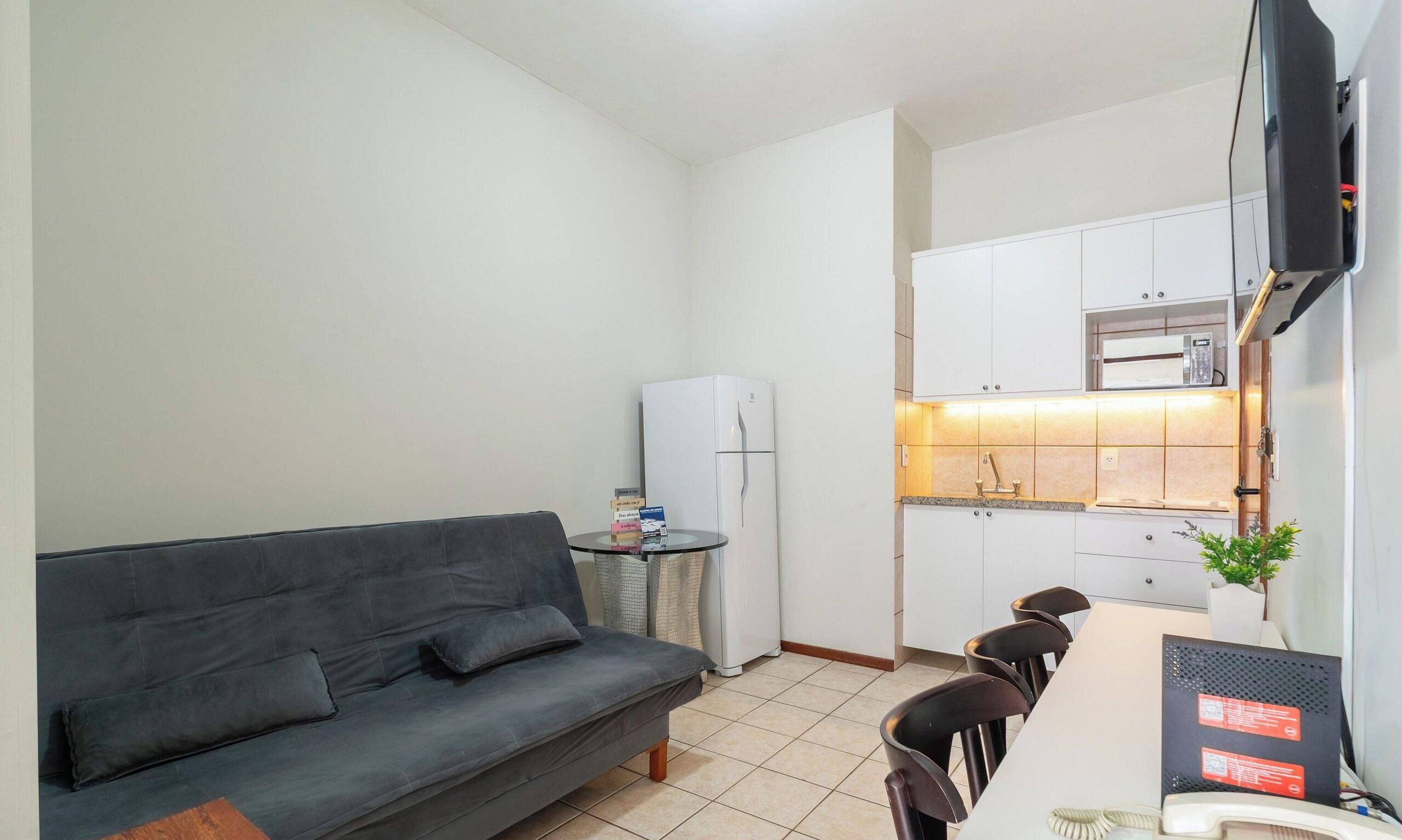 Un espacio habitable compacto con sofá, una pequeña mesa de comedor, refrigerador y una zona de cocina con armarios y microondas.