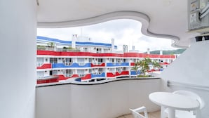 A balcony with a view of a multi-story building with balconies painted in red, white, and blue. There is a white table and two white chairs on the balcony. - Apartment 200m From Ingleses Beach Iho264 (Florianópolis)