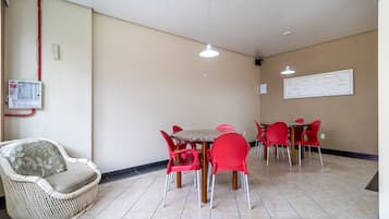 Un comedor con una mesa redonda y sillas rojas, un sofá de mimbre y un panel eléctrico fijado a la pared.