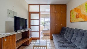 Een woonkamer met een televisie, houten kasten, een bank en een schilderij aan de muur.