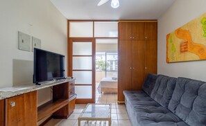 A living room with a TV, wooden cabinets, a sofa, and a painting on the wall. - Apt c/ Varanda in Condominio Pe na Areia Iho127 (Florianópolis)