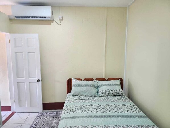 A bedroom with a bed, a door, and an air conditioning unit.