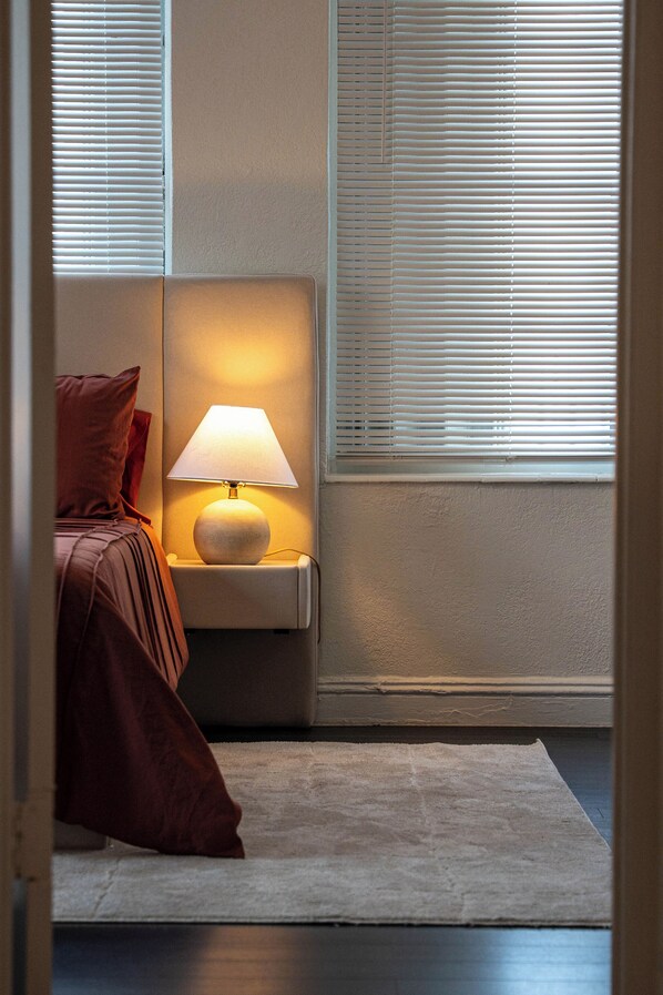 Une chambre à coucher avec un lit, une table de chevet avec une lampe et une fenêtre avec des stores.