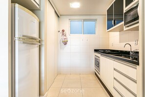 A compact kitchen with a refrigerator, stove, and a window. - Comfortable Apart 400 m From the Beach Idp104 (Florianópolis)