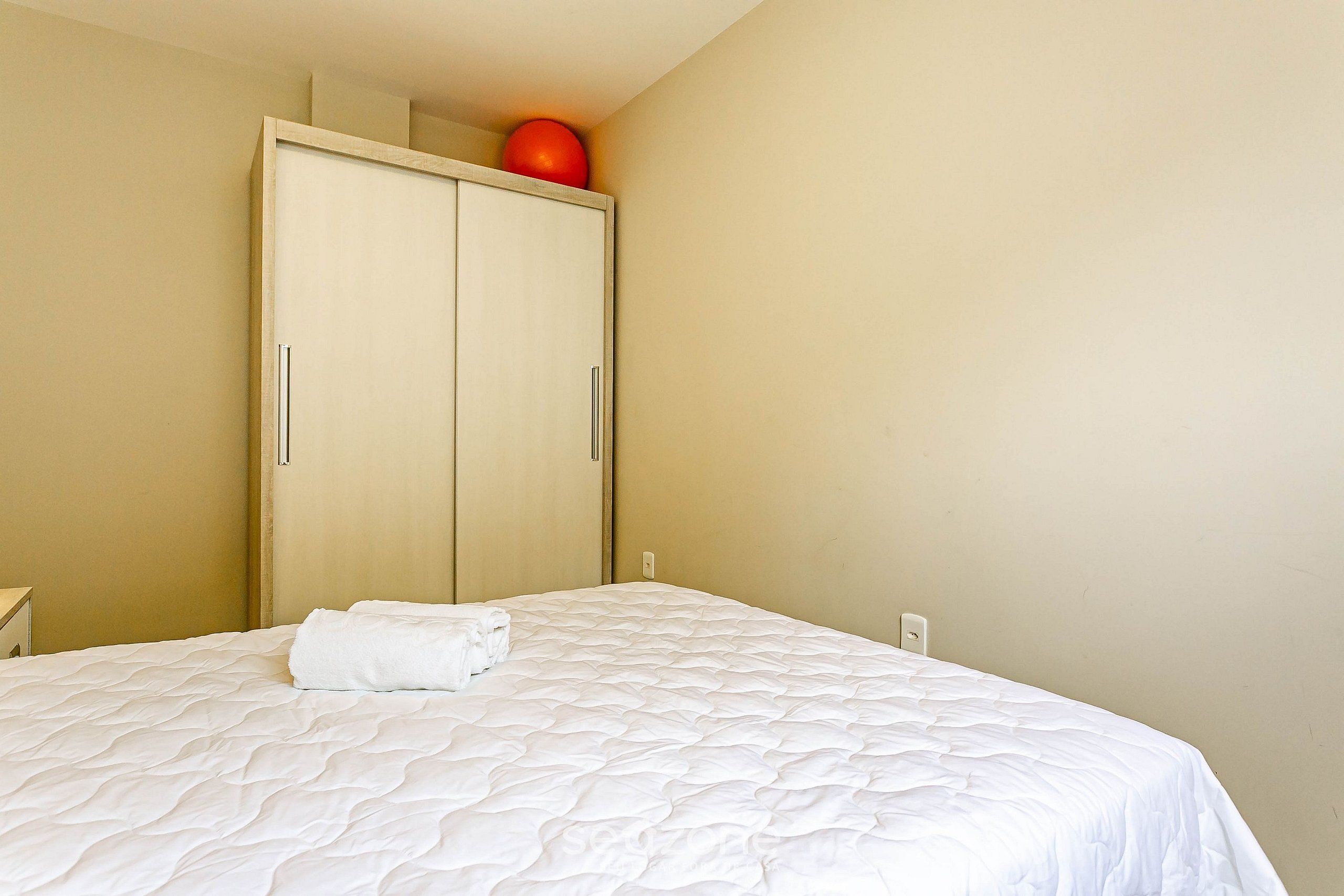 Une chambre d’hôtel avec un lit, une armoire et un objet rouge posé sur le dessus de l’armoire.