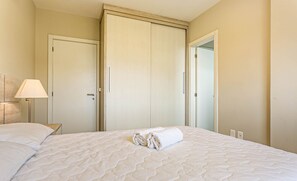 Un lit bien fait, avec une serviette pliée, une lampe de chevet et une armoire aux portes coulissantes.