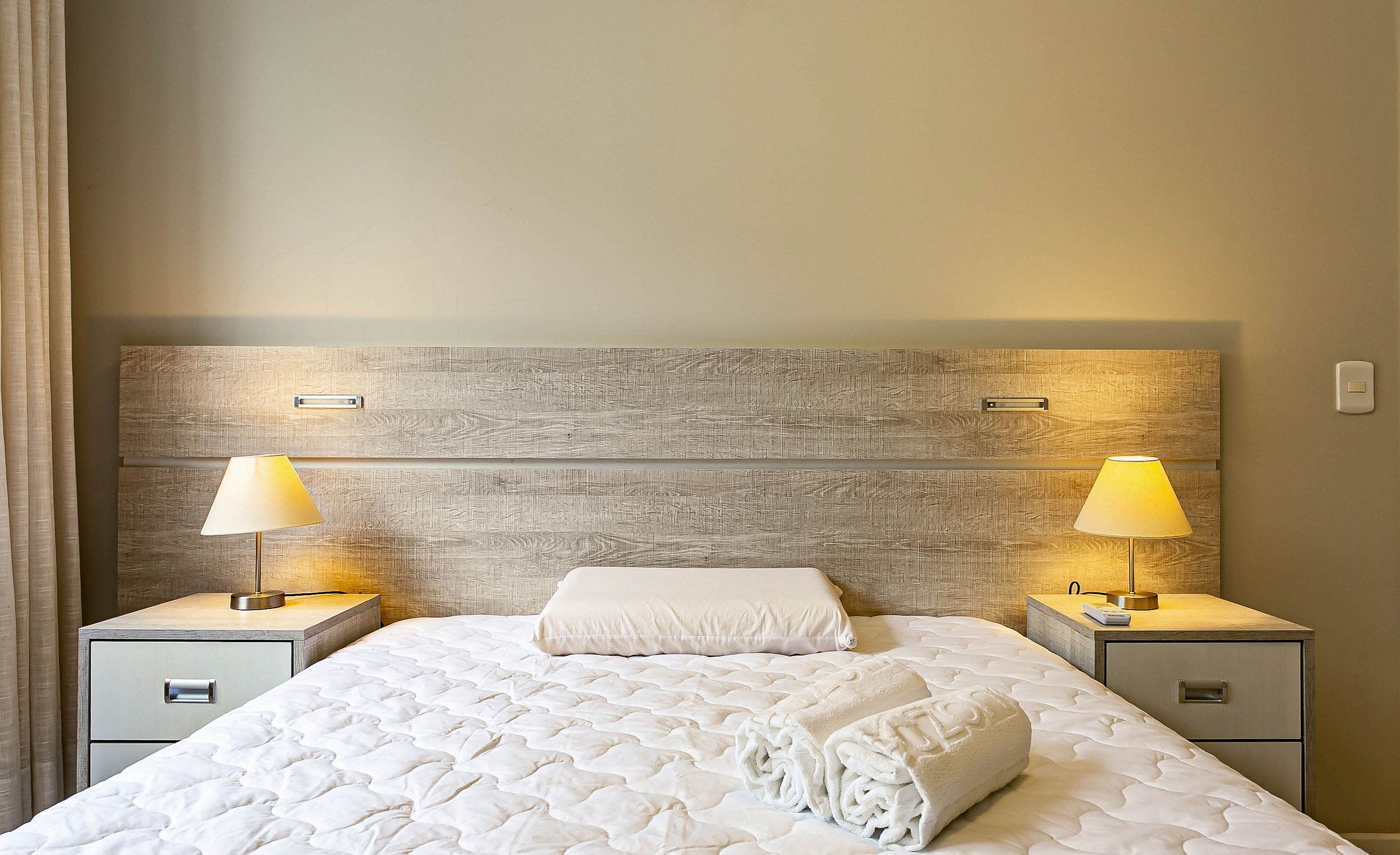 Una cama bien hecha con un cubrecolchón acolchado, dos mesitas de noche con lámparas y un cabecero de madera.