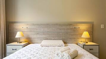Una cama bien hecha con un cubrecolchón acolchado, dos mesitas de noche con lámparas y un cabecero de madera.