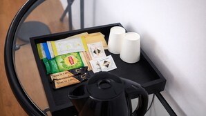 Una pequeña bandeja negra con una cafetera, bolsitas de té y dos velas blancas sobre una mesa.