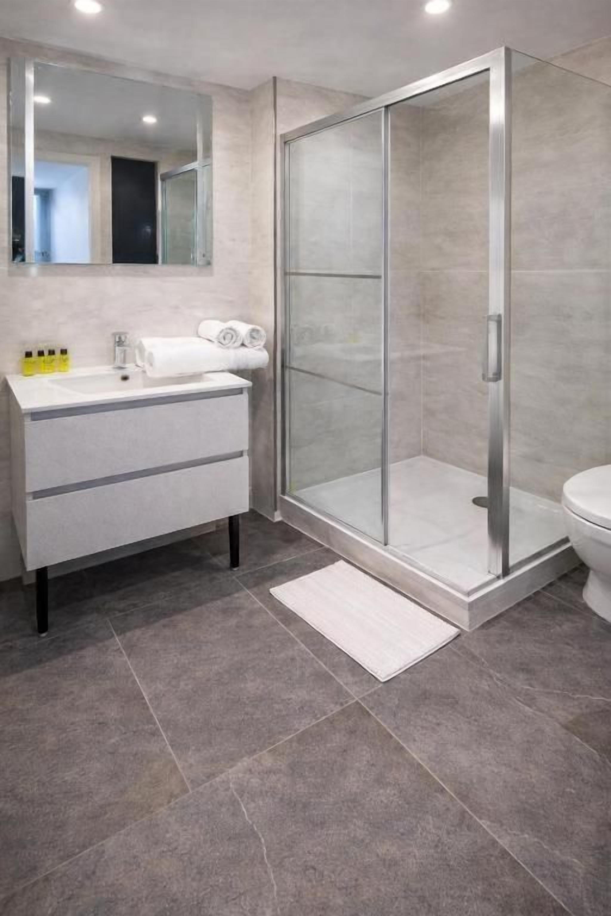 A modern bathroom with a glass shower enclosure, a white sink, and a toilet.