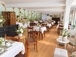 Un comedor amplio con varias mesas y sillas, un mueble negro y plantas decorativas.