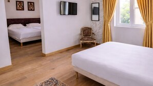 Un dormitorio con cama, una silla, un televisor y una ventana con cortinas.