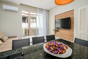 Quarto de hotel moderno com área de jantar, televisão de tela plana na parede e varanda com porta de correr.