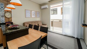 A modern kitchen with a dining area, a sofa, and a large window with a view. - Apart Foot on Sand for Couples in Floripa Ida105 (Florianópolis)