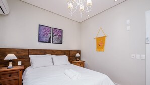 A neatly made bed with white linens, two bedside lamps, a wooden nightstand, and a wall-mounted decorative piece. - Apart Foot on Sand for Couples in Floripa Ida105 (Florianópolis)