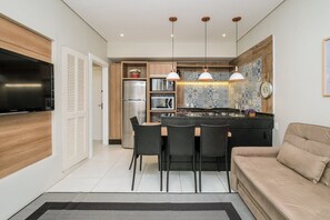Cozinha moderna com área de jantar, apresentando uma televisão grande, armários de madeira e luminárias pendentes.