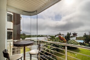 A balcony with a table and chairs, overlooking a swimming pool and lush greenery. - Excellent Beachfront apt With Barbecue Ida101 (Florianópolis)
