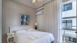 A hotel room with a bed, a nightstand, a lamp, an air conditioning unit, a window with curtains, and a balcony. - Excellent Beachfront apt With Barbecue Ida101 (Florianópolis)