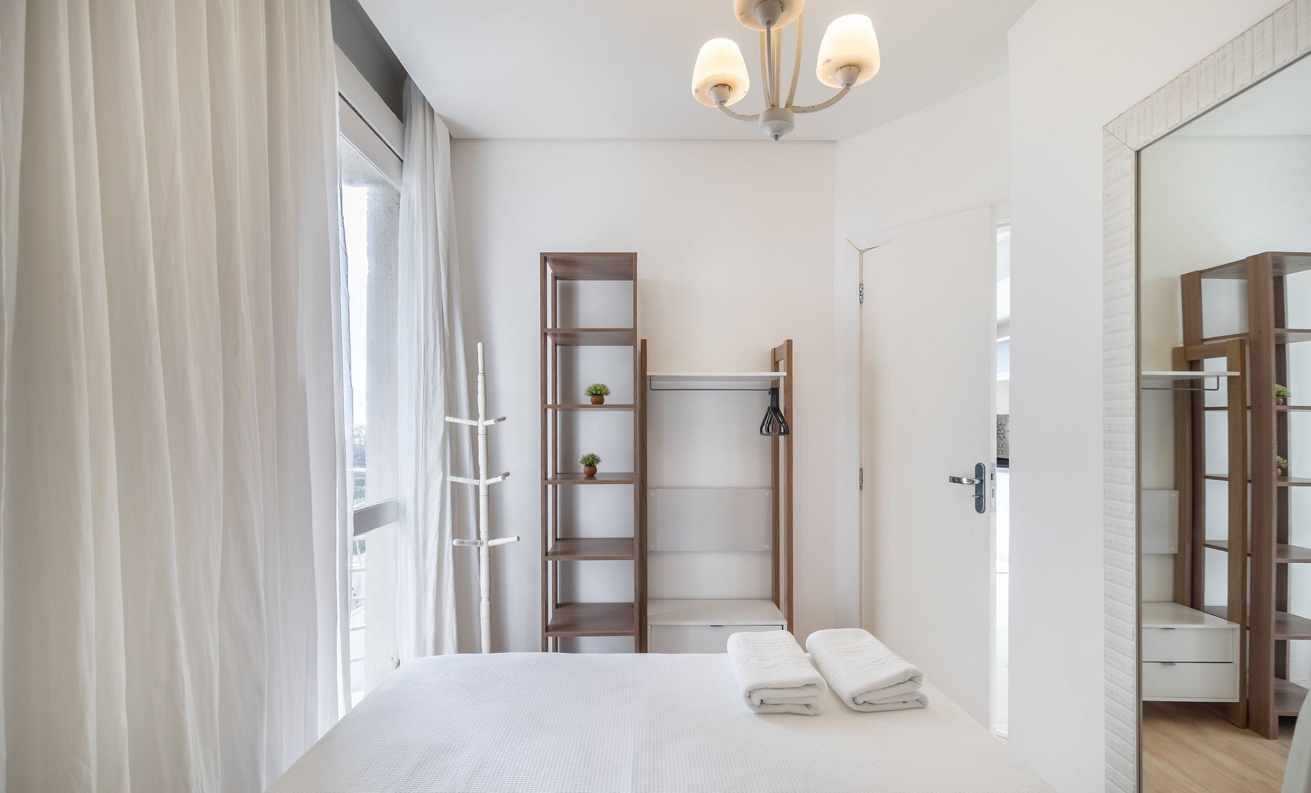 A modern bedroom with a large bed, a wooden ladder, a small shelf with plants, and a mirror.