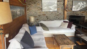 A cozy room with a stone wall, a white sofa, a wooden coffee table, and a TV.