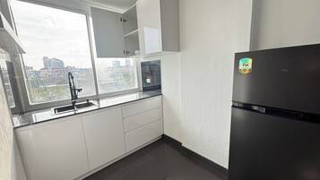 A modern kitchen with a black refrigerator, white cabinets, and a window with a view of buildings.