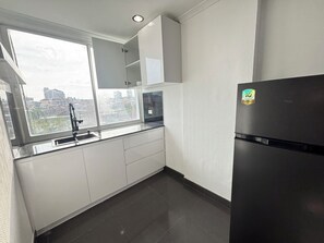 Una cocina moderna con un refrigerador negro, gabinetes blancos y una ventana con vistas a edificios.