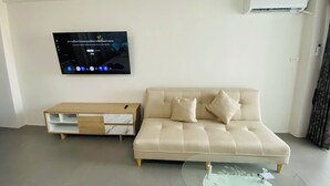 Una sala moderna con un sofá color beige, una mesa de centro de vidrio y un televisor de pantalla plana montado en la pared.