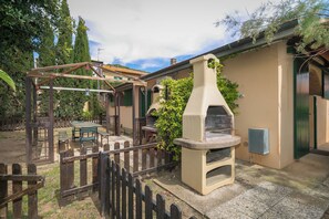 Eine Terrasse mit einer Holz-Pergola, einem Steinofen und einem Tisch mit Stühlen.