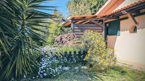 A garden with various plants and flowers, a wooden pergola, and a building with a tiled roof.