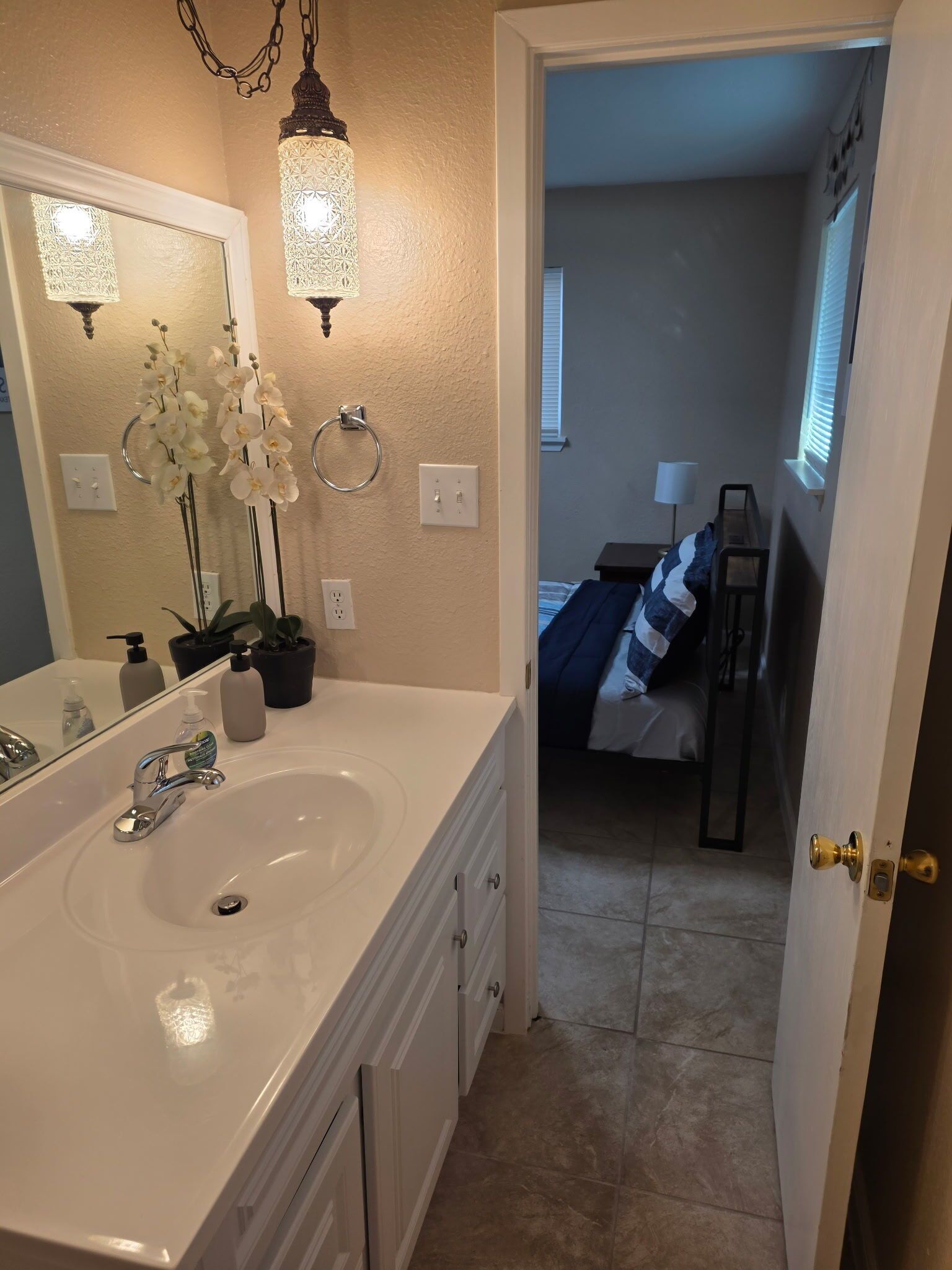 Une salle de bain avec un lavabo blanc, deux appliques murales, un miroir et une orchidée en pot.