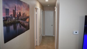 A hallway with a cityscape painting, a white door, and a thermostat on the wall. - Cozy Newly Renovated 3 Bedroom Home 5 min. to SoCo & 15 min. to Zilker Park (Austin)
