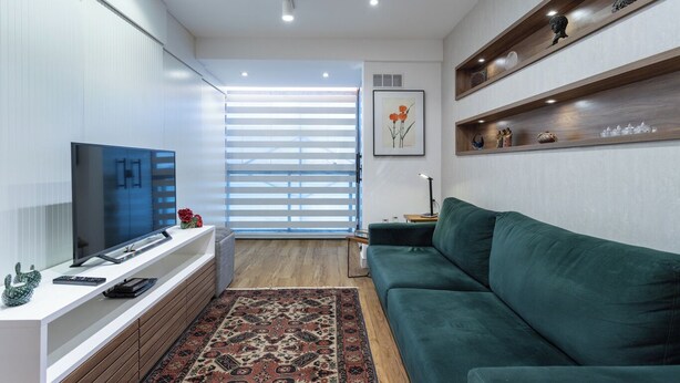 Un soggiorno moderno con una televisione a schermo piatto, un divano verde, un mobile in legno e un tappeto decorato.