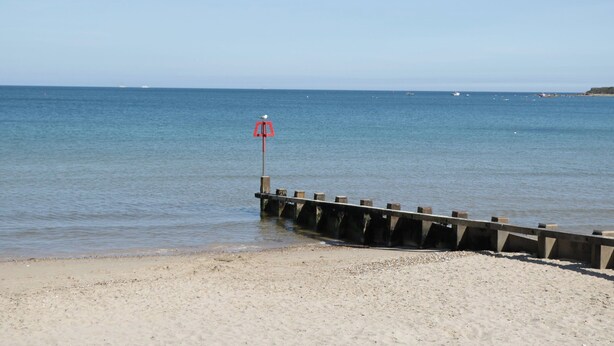A beach with a wooden pier extending into calm waters, a lifebuoy on the pier, and a clear sky. - Flat 9 (Swanage)