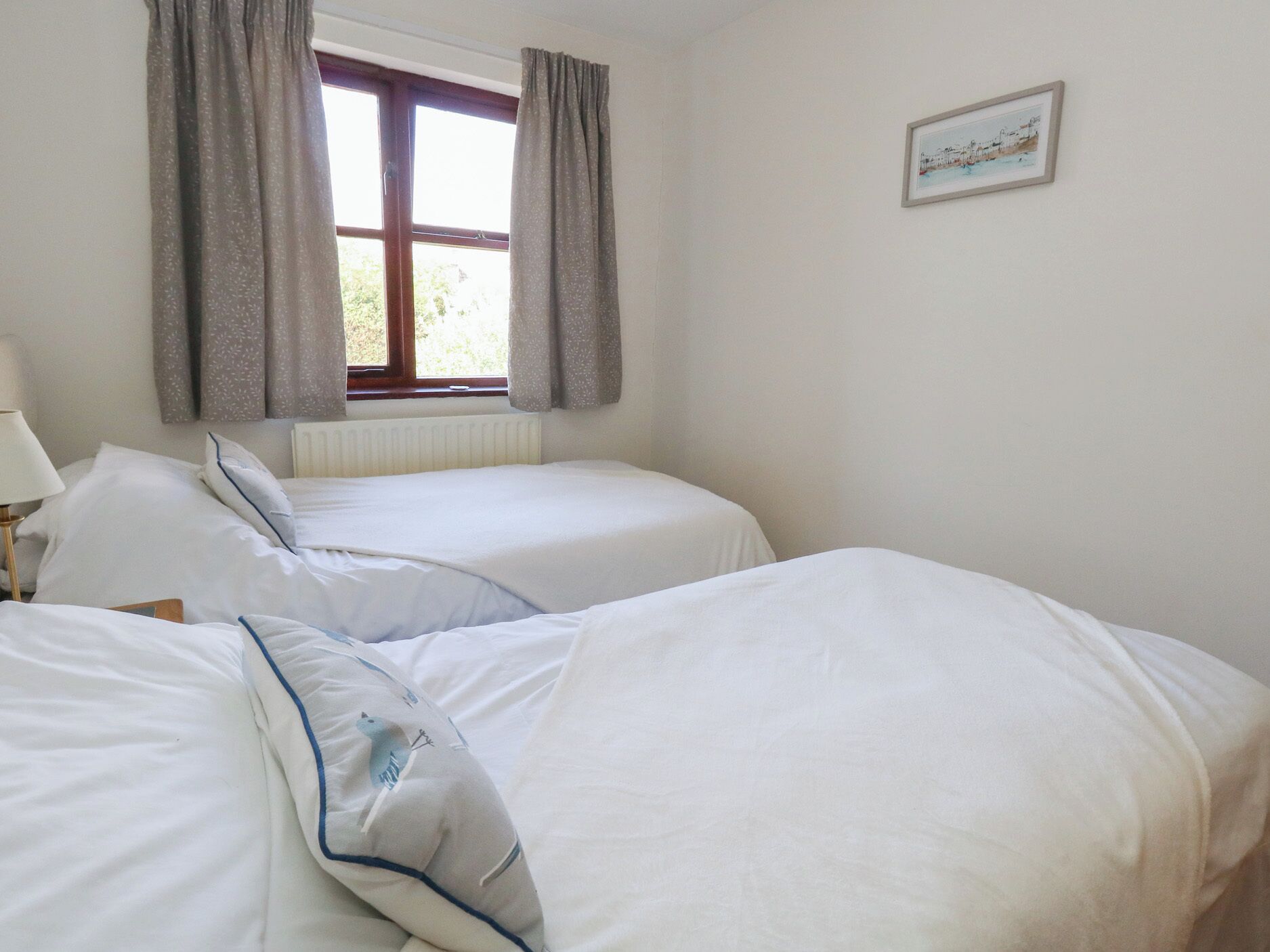 A bedroom with two beds, a window with curtains, a radiator, and a framed picture on the wall.