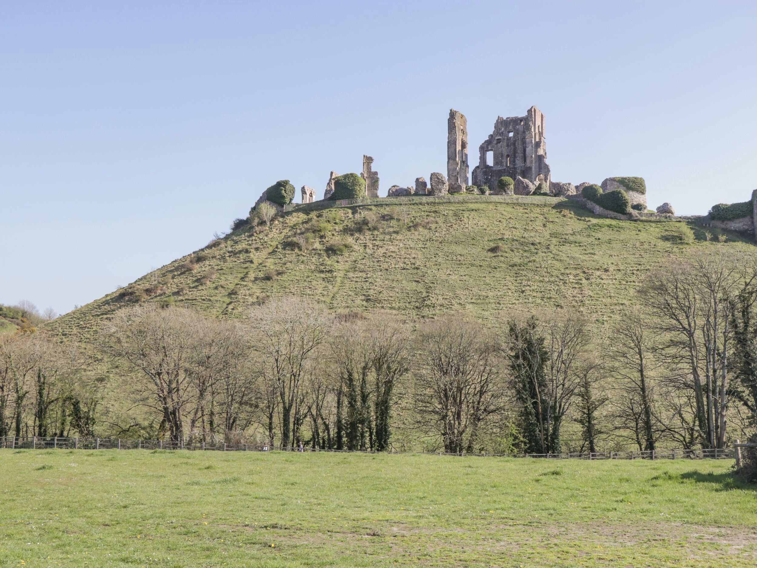 A hill with ruins at the top, surrounded by trees and open fields.