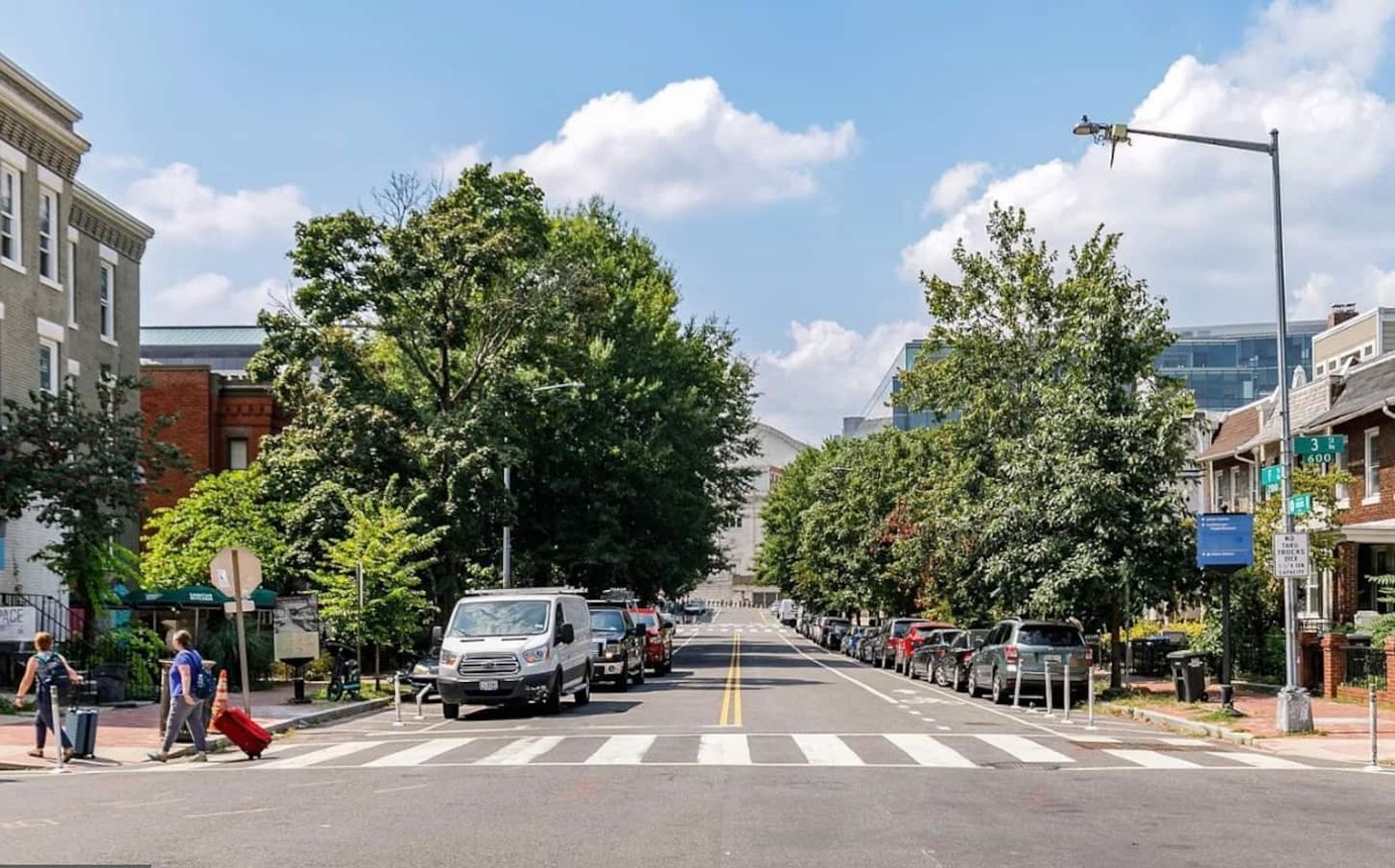 A street lined with parked cars and trees, with buildings on either side.