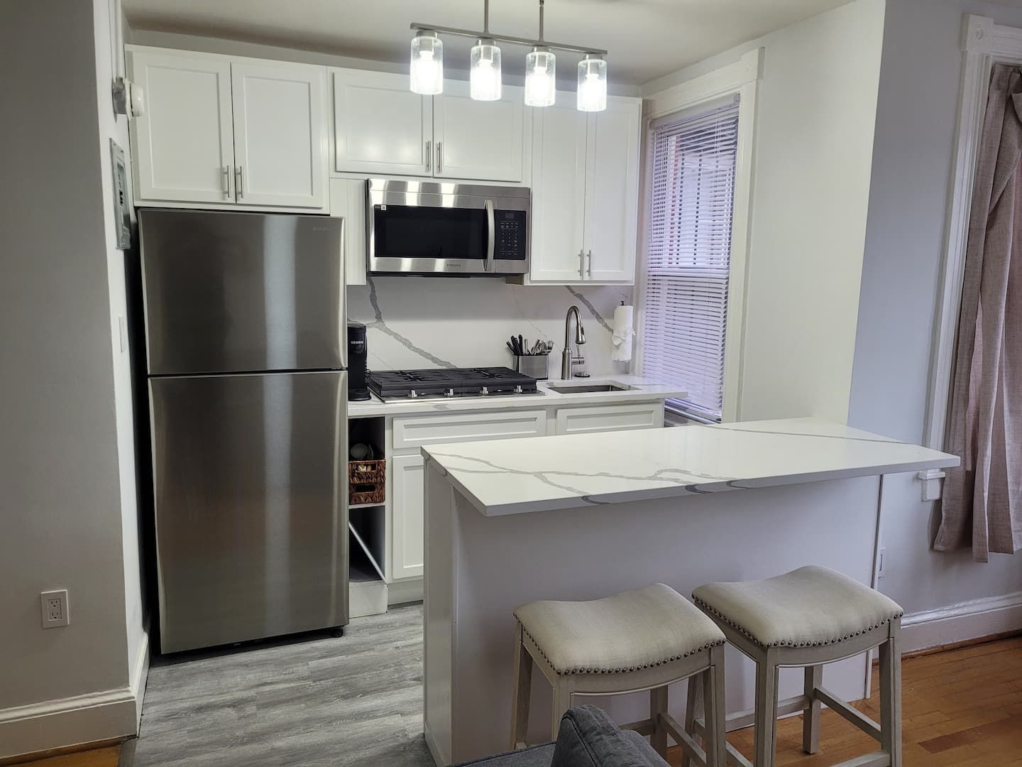 A modern kitchen with white cabinetry, stainless steel appliances, and a central island with stools.