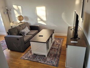 Een woonkamer met een bank, salontafel, tv-meubel en vloerkleed.