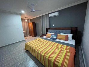 A hotel room with a large bed, a ceiling fan, and an air conditioning unit.
