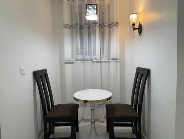 A small round table with two chairs, a window with curtains, and wall-mounted lights.