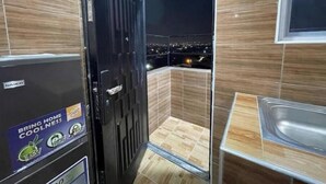 Une petite salle de bain avec une porte noire, une petite fenêtre et une vue sur le paysage urbain la nuit.